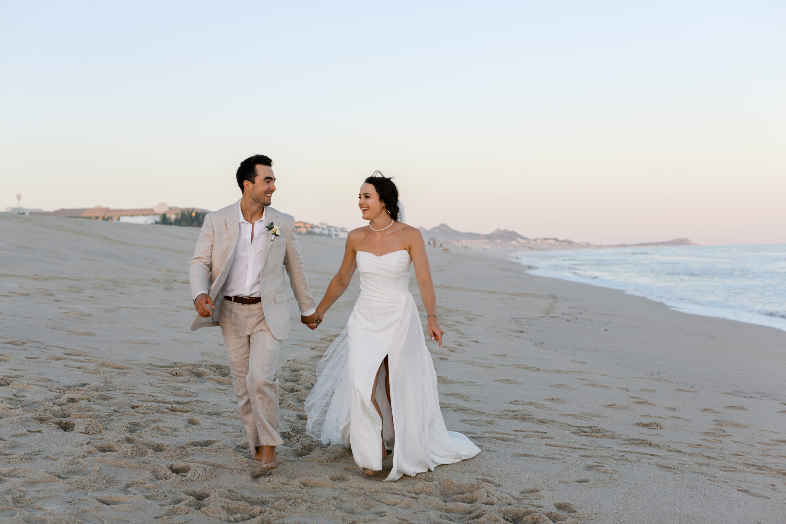 Bride and groom walking barefoot on the beach at sunset during their Hyatt Ziva Los Cabos wedding in Cabo San Lucas.